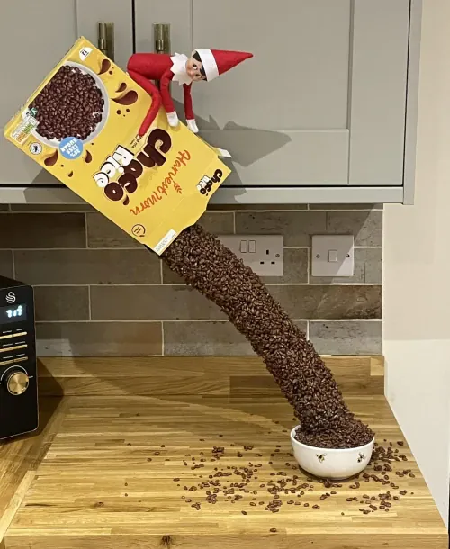 Elf on the Shelf pouring cereal into a bowl with pool noodle